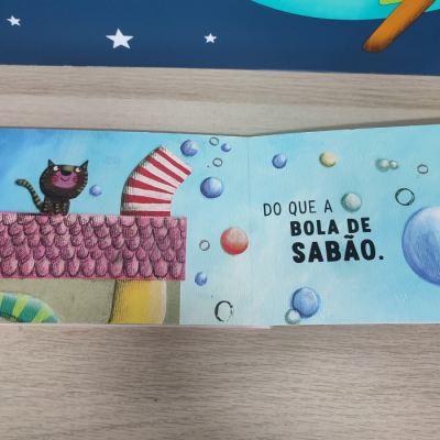 Página de livro infantil com gato no telhado, bolhas de sabão e texto em português.