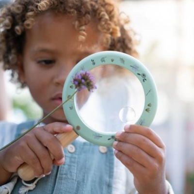 Criança com lupa verde clara a observar flor roxa