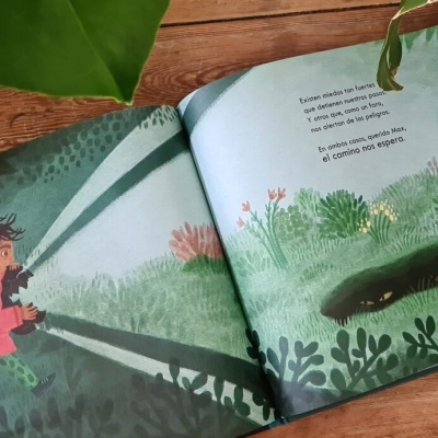 Livro infantil aberto com ilustrações e texto, rodeado por folhas e madeira