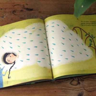 Livro aberto com ilustração de pessoa sob manta branca com manchas azuis