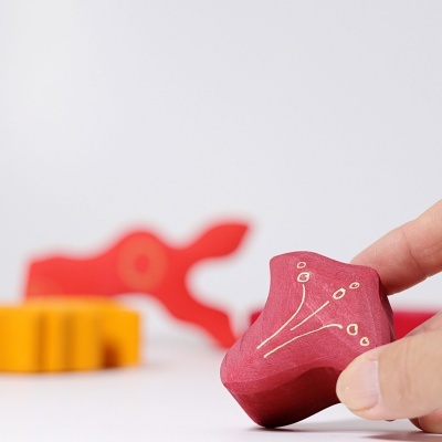 Peça de madeira vermelha decorada e mão a segurá-la com outras peças coloridas desfocadas ao fundo