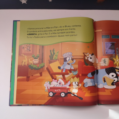 Página de livro infantil com cães coloridos numa sala de estar com texto em português