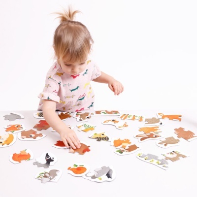 Criança pequena a montar puzzle de madeira com animais em superfície branca