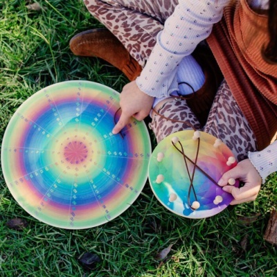 Dois instrumentos musicais coloridos em arco-íris com cordas e pinos, sobre relva, mãos de criança a tocar