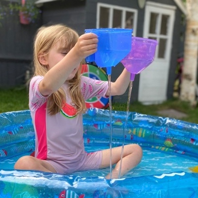 Criança em piscina insuflável azul a verter água de balde azul para balde roxo