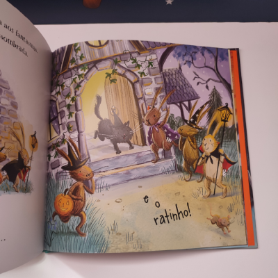 Página ilustrada de livro infantil com coelhos à porta de uma casa e texto 'é o ratinho!'