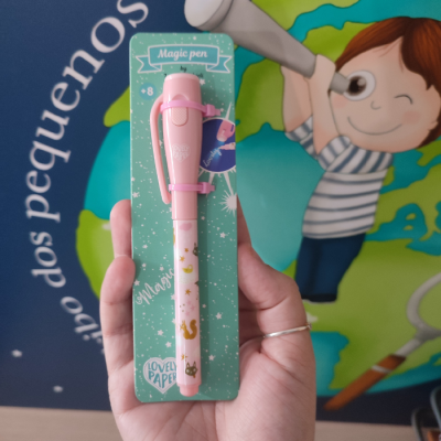 Caneta mágica cor-de-rosa com padrões dourados em cartão verde com texto, segurada por mão com fundo ilustrado.