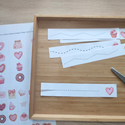 Recortes de papel com linhas pontilhadas e folha com adesivos de cupcakes e corações numa bandeja de madeira.