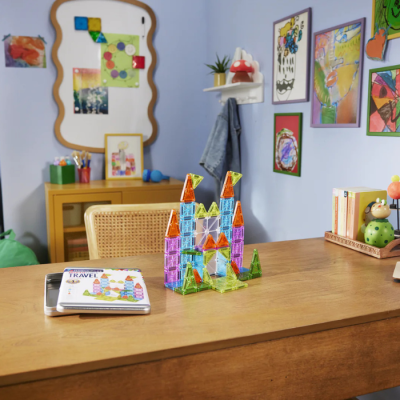Castelo de peças magnéticas coloridas numa mesa de madeira com caderno metálico com texto TRAVEL ao lado