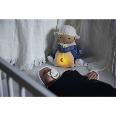 Boneco de peluche ovelha com luz interior perto de bebé no berço