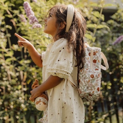 Criança com vestido de bolinhas e mochila floral num jardim