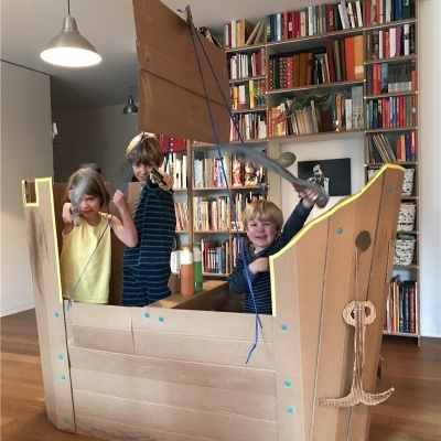 Barco de brincar de cartão com crianças numa sala com estantes e livros