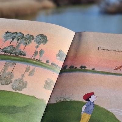 Livro aberto com ilustrações de pessoas e paisagem junto a lago