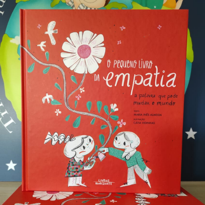 Capa de livro vermelho com ilustração de duas crianças e flor branca, título O pequeno livro da empatia