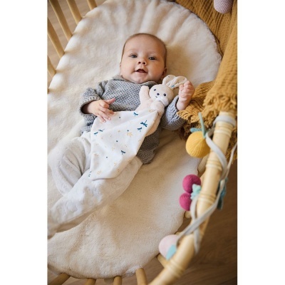 Bebé deitado numa cama oval de madeira com manta felpuda e brinquedo de coelho de pano