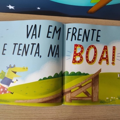 Livro aberto com ilustração de crocodilo, campo verde e texto motivacional