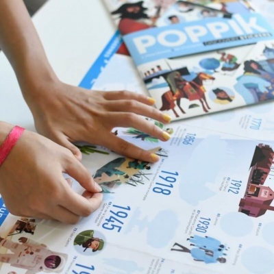 Mãos tocando papeis ilustrados com figuras e datas históricas e capas de revistas POPPIK