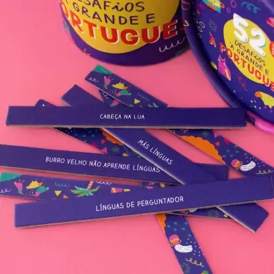 Jogo de 52 desafios a grande em português com tiras coloridas com frases em português sobre superfície cor-de-rosa