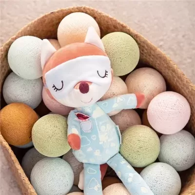 Peluche de raposa azul claro numa cesta com bolas decorativas em tons pastel