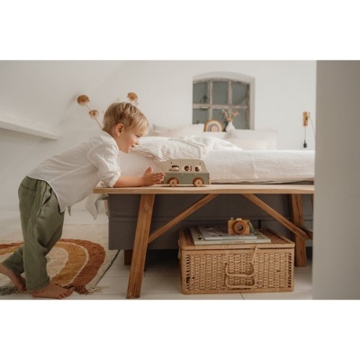 Criança a brincar com carro de madeira numa cama de madeira clara com manta branca num quarto acolhedor