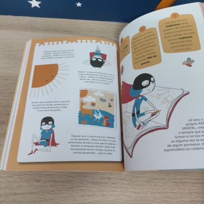 Livro ilustrado aberto sobre mesa de madeira clara com fundo azul e estrelas brancas