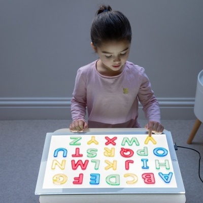 Criança a brincar com letras de madeira coloridas numa mesa de luz branca
