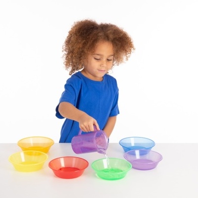 criança a verter água em tigela verde com copo roxo