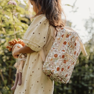 Criança com mochila floral bege ao ar livre.