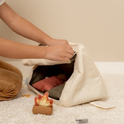 Saco triangular de tecido bege com almofadas coloridas e brinquedo de fogo junto num tapete branco