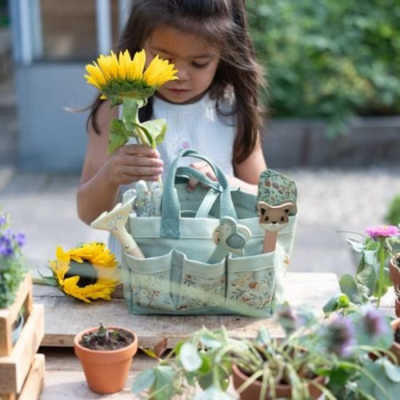Criança segurando girassol com bolsa de jardim de tecido e ferramentas de brinquedo em mesa com plantas