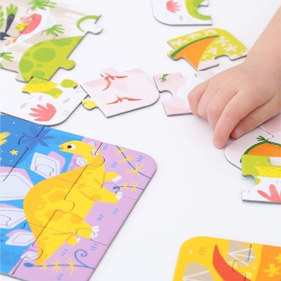 Peças de puzzle infantil colorido com dinossauros e uma mão a encaixar uma peça.