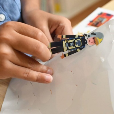 Mãos a segurar figura de bombeiro em papel numa mesa de madeira.