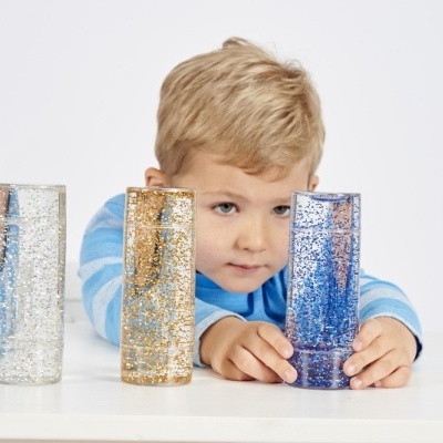 Três tubos sensoriais com glitter em três cores e uma criança a manipular um deles.