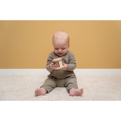 Bebé com roupa cinza claro segurando brinquedo de madeira num tapete branco