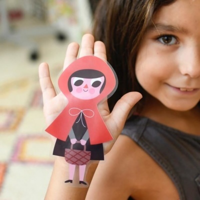 Desenho colorido de personagem infantil com capuz vermelho na mão de uma criança.