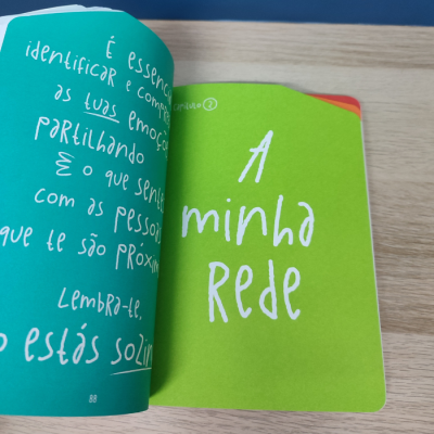 Livro aberto com páginas verdes e azuis contendo texto manuscrito em português