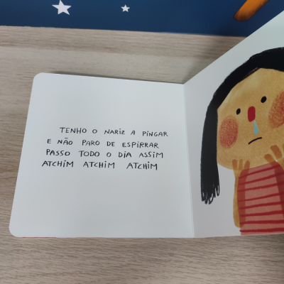 Página aberta de livro infantil com texto manuscrito e ilustração de criança com nariz a pingar