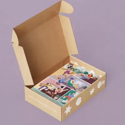 Caixa de papelão castanho aberta com três cartões ilustrados coloridos dentro e desenhos de conchas e estrelas do mar na lateral