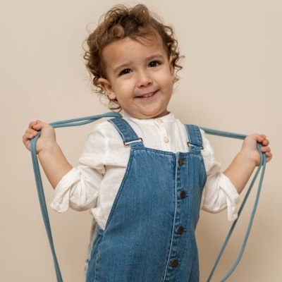Criança com camisa branca e jardineira azul segura cordão azul
