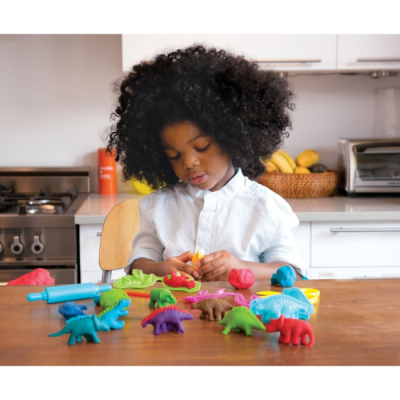 Criança a brincar com dinossauros de massinha colorida numa cozinha moderna