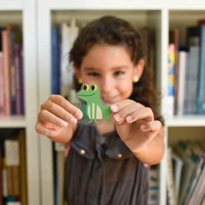 Criança segurando um autocolante de sapo verde na frente de uma estante de livros