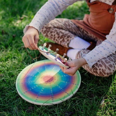 Brinquedo de madeira colorido em mãos de criança sentada na relva com calças animal print e top laranja