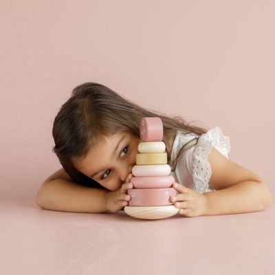Criança segurando brinquedo empilhável de madeira em tons pastel rosa e creme