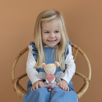 Menina com vestido azul e t-shirt branca a segurar uma boneca de tecido numa cadeira de bambu