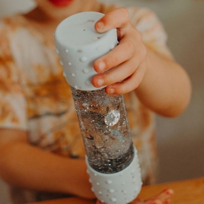 Garrafa de água transparente com tampa e base cinzentas com textura de pontos na mão de uma criança