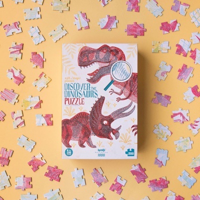 Caixa de puzzle de dinossauros com peças espalhadas sobre fundo amarelo