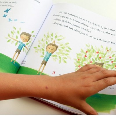 Livro infantil colorido aberto com ilustrações e texto em português, mão de criança a segurar