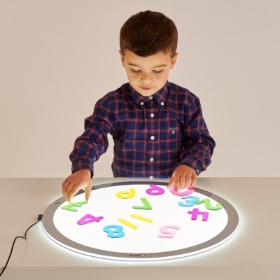 Menino a jogar com números de plástico coloridos numa mesa iluminada
