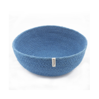 Cesto redondo azul trançado com etiqueta branca numa superfície branca