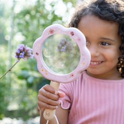 Criança a segurar lupa infantil flor cor-de-rosa com desenhos, cabo de madeira num jardim.